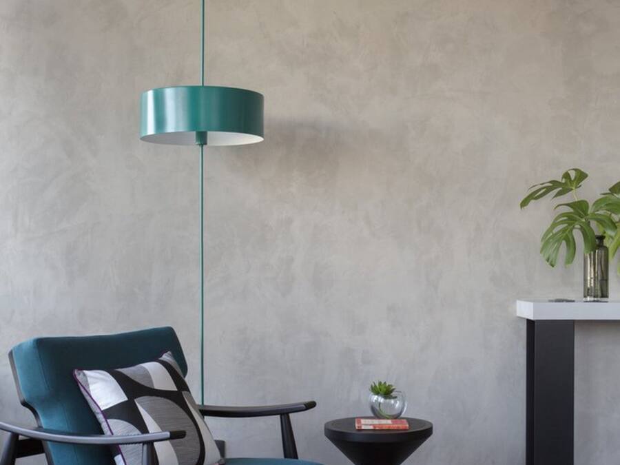 A modern room with a teal chair, a black and white rug, a round black table with a plant, and a teal pendant light.