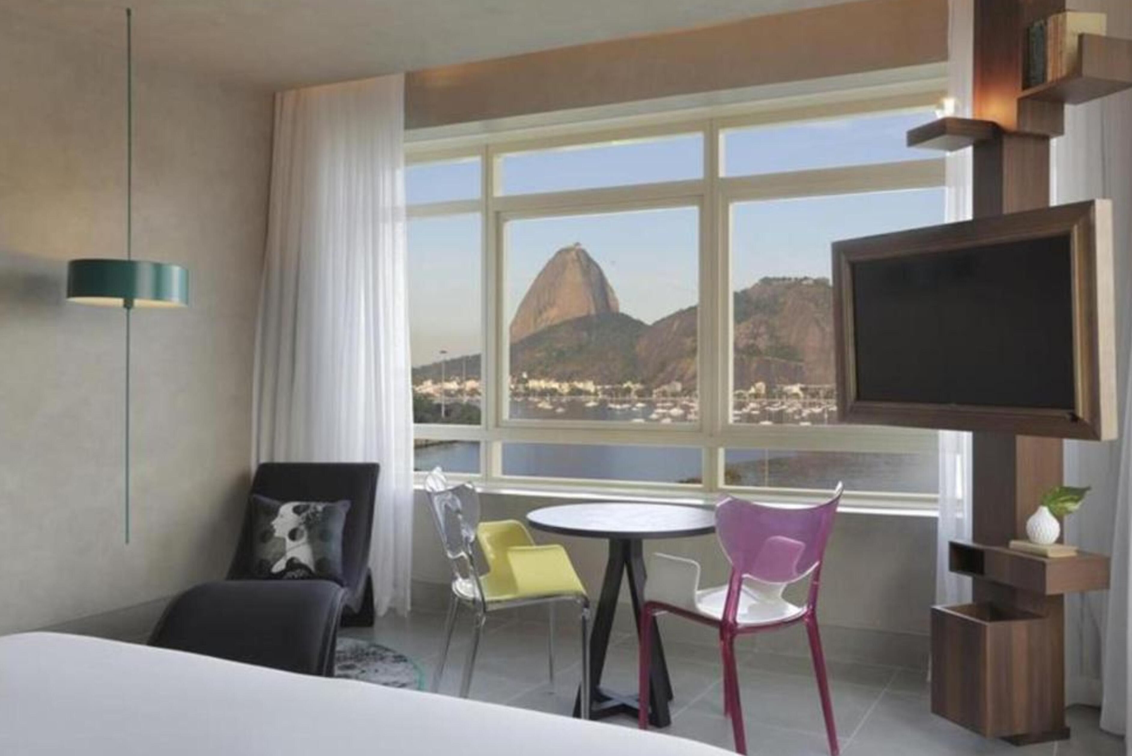 A hotel room with a bed, a TV, a window with a view of a mountain, and a table with chairs.