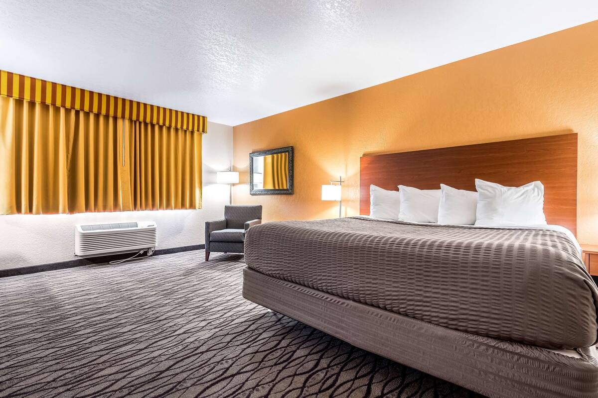 A hotel room with a large bed, a chair, a desk, and a window with curtains.