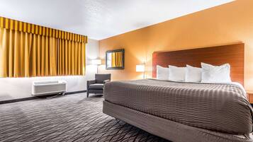 A hotel room with a large bed, a chair, a desk, and a window with curtains.