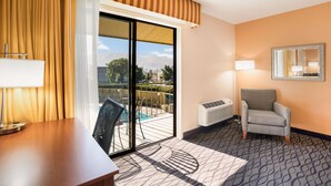 Una habitación de hotel con un escritorio de madera, una silla, un ventanal con cortinas y vistas a montañas, además de una alfombra estampada.