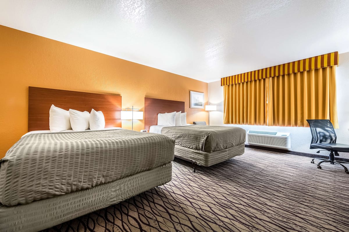A hotel room with two beds, a desk, and a window with curtains.