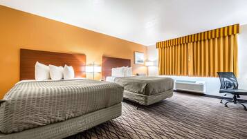 A hotel room with two beds, a desk, and a window with curtains.