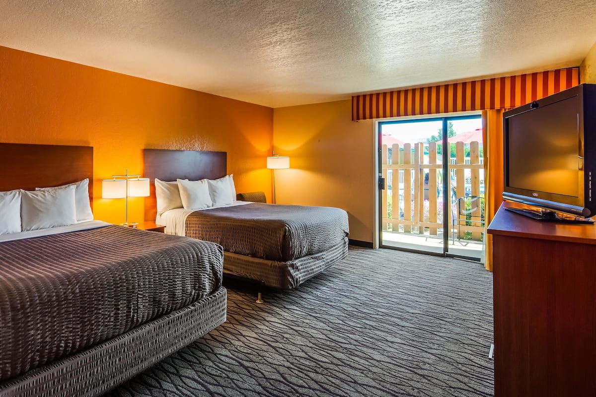 A hotel room with two beds, a television, and a sliding glass door to the outside.