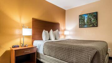 A hotel room with a bed, bedside lamps, a nightstand with a radio, and a painting on the wall.