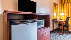 Habitación de hotel compacta con kitchenette, televisor de pantalla plana, microondas, escritorio con silla y lámpara de noche.