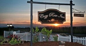 A sign for Cozy Rose Inn with a sunset in the background.