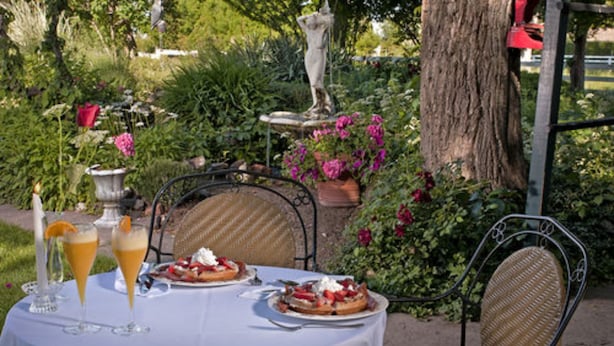 Une table dressée à l’extérieur, recouverte d’une nappe blanche, avec deux assiettes de nourriture et deux verres contenant une boisson jaune.