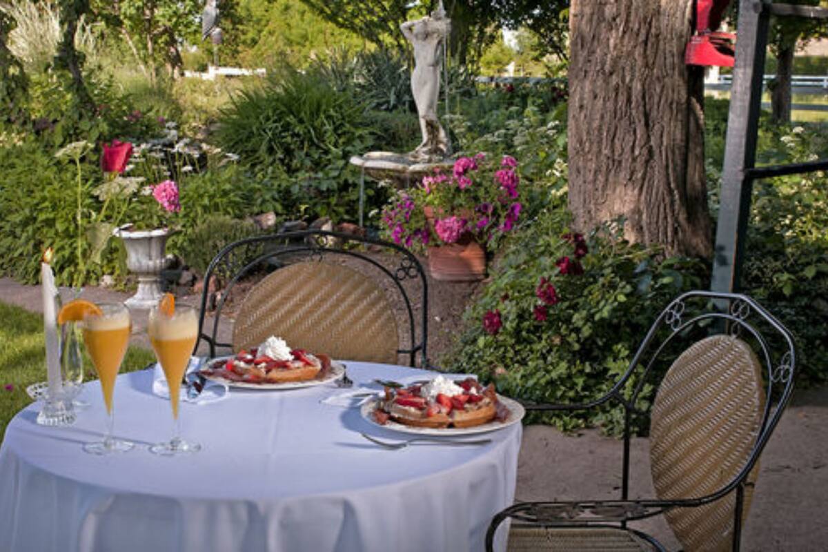 A table set outdoors with a white tablecloth, two plates of food, and two glasses of a yellow beverage.