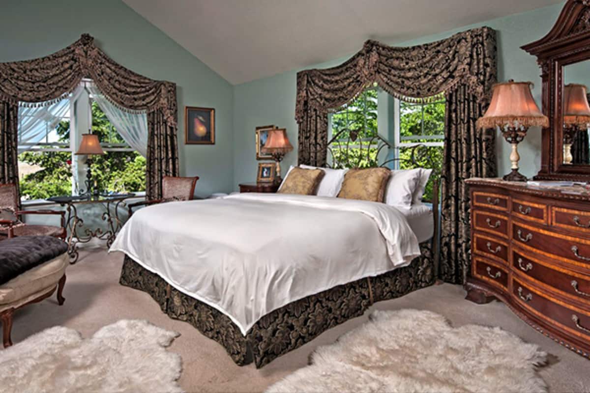 A bedroom with a large bed, a dresser, a chair, and a lamp.