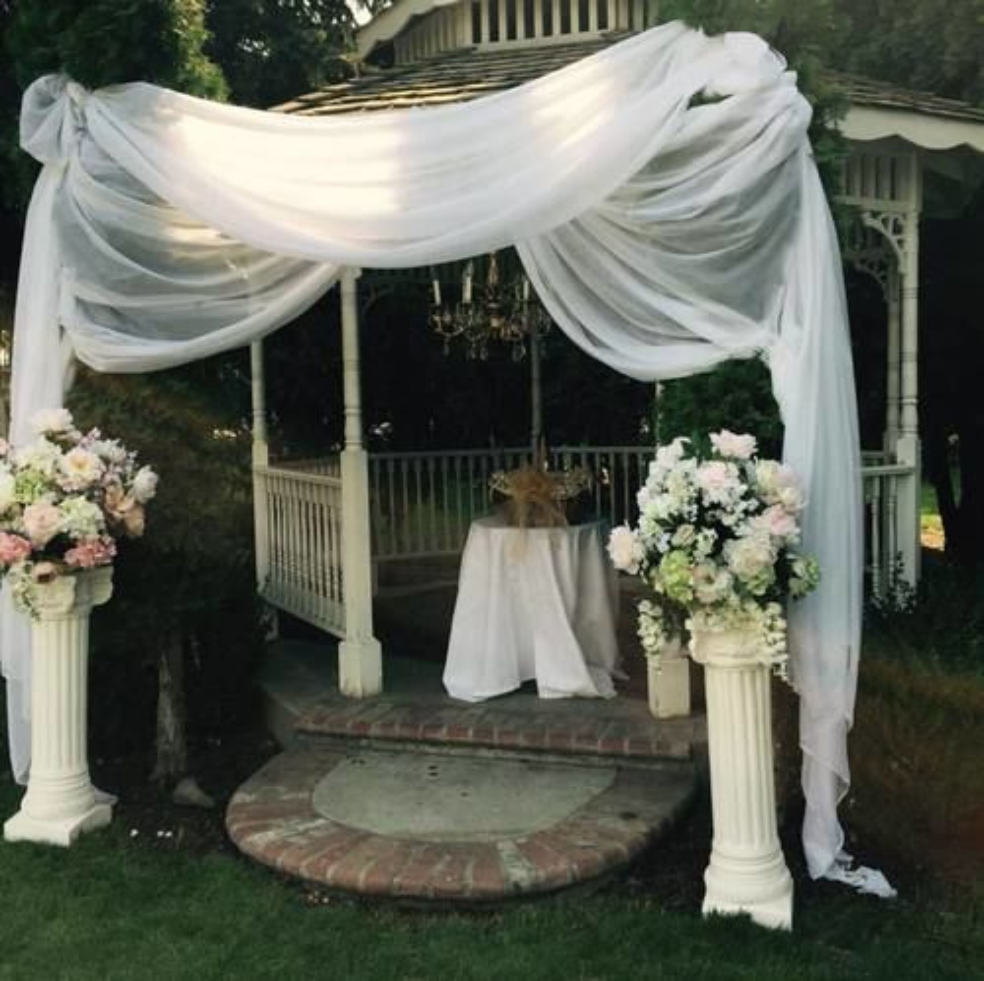 A gazebo with white drapery and floral arrangements.