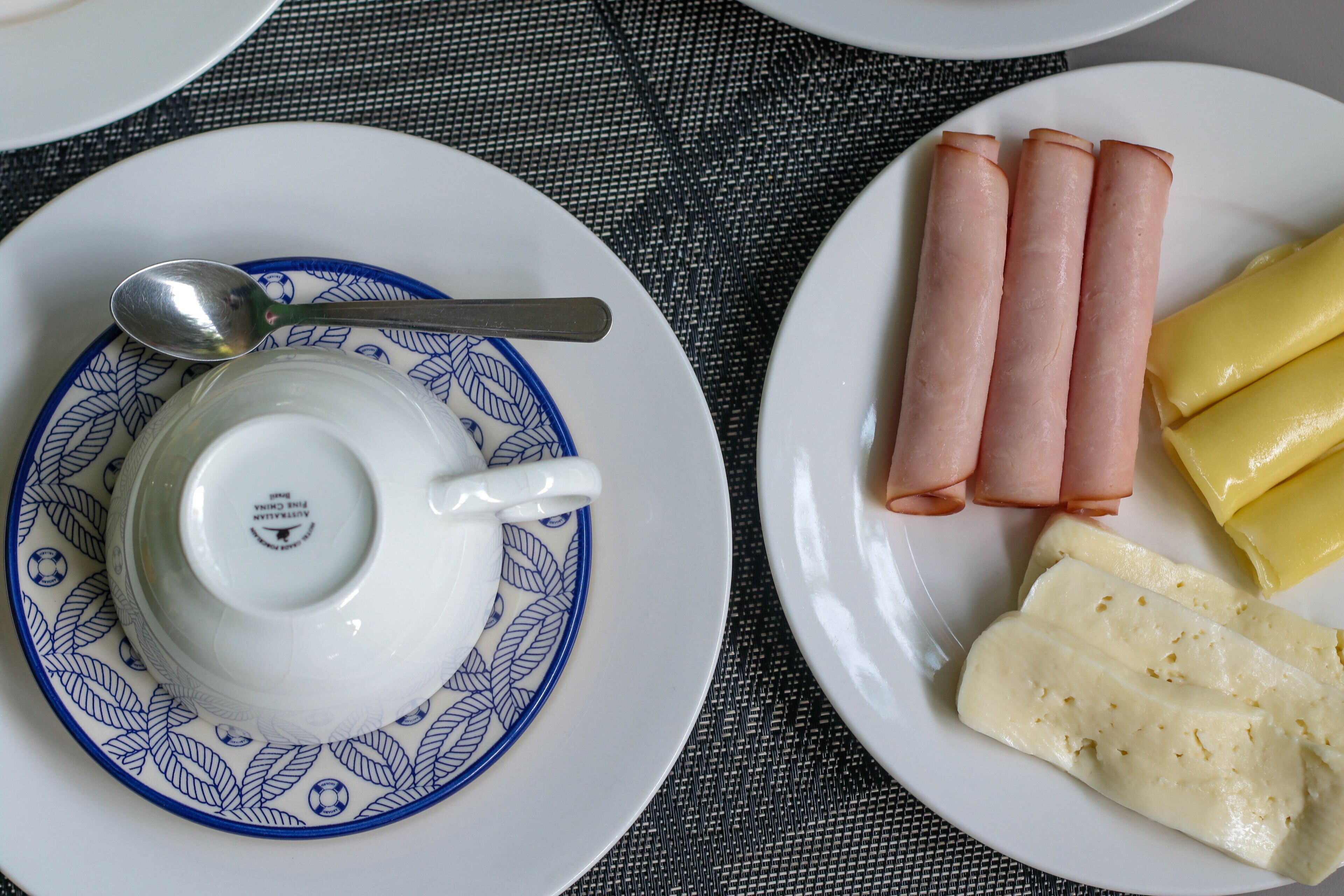 Two plates with food items, one with a spoon and a teapot on a patterned saucer.