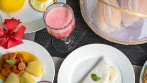 A table set with various breakfast items including pancakes, eggs, and fruit, along with a pitcher of juice. - Pousada Leão Marinho (Fernando de Noronha)