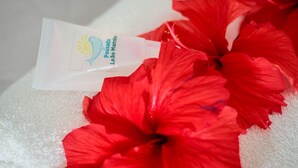 A tube of sunscreen with a sun and water wave logo, placed on a white towel with red hibiscus flowers. - Pousada Leão Marinho (Fernando de Noronha)