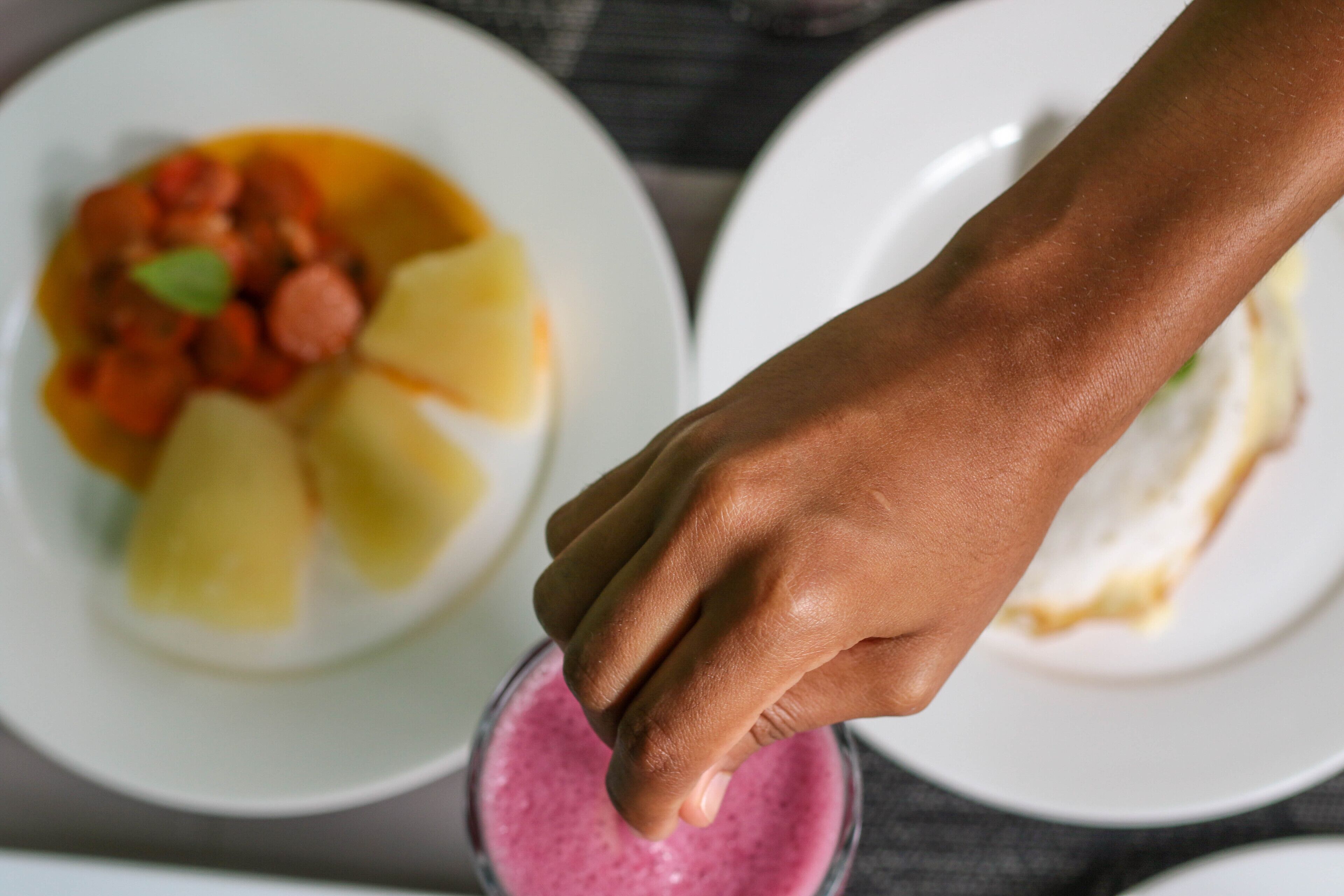 Una mano sosteniendo una bebida, con dos platos de comida al fondo.