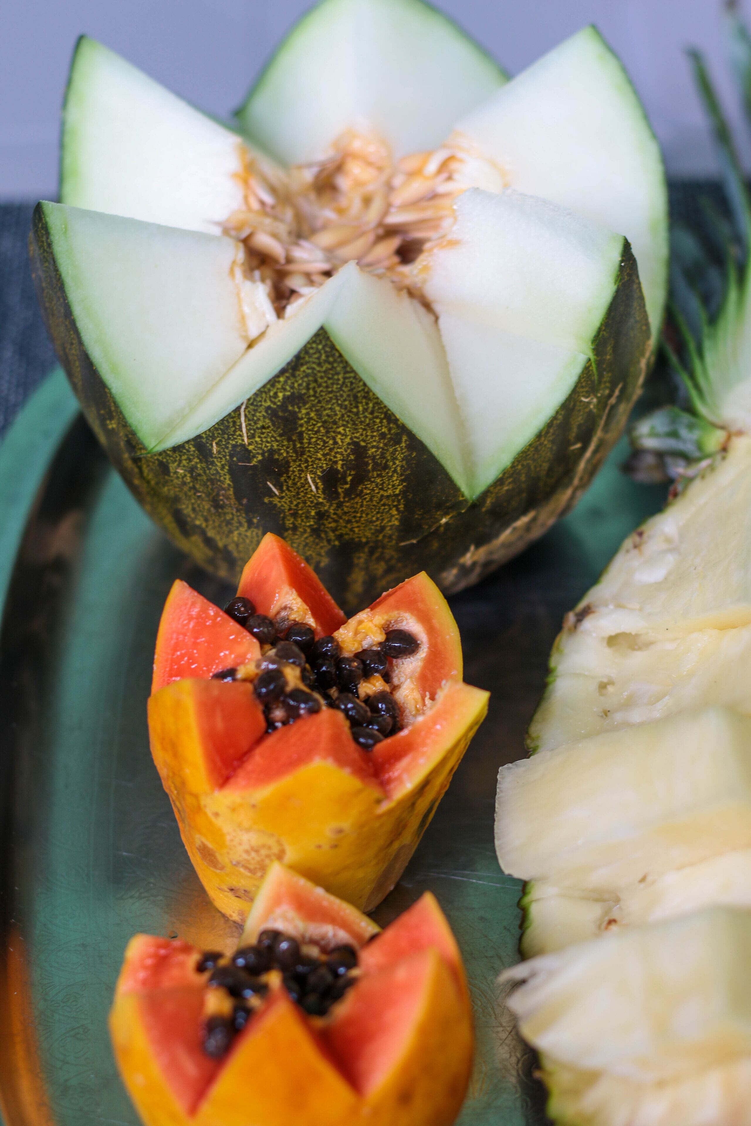 A fruit platter with sliced papaya, pineapple, and a whole melon.