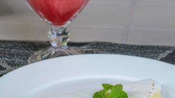 A dessert with a slice of cake topped with a mint leaf, a glass of pink beverage, and a stone wall in the background.