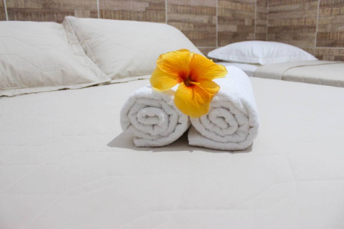 Un lit bien fait, avec du linge de lit blanc et une fleur jaune posée sur le dessus.