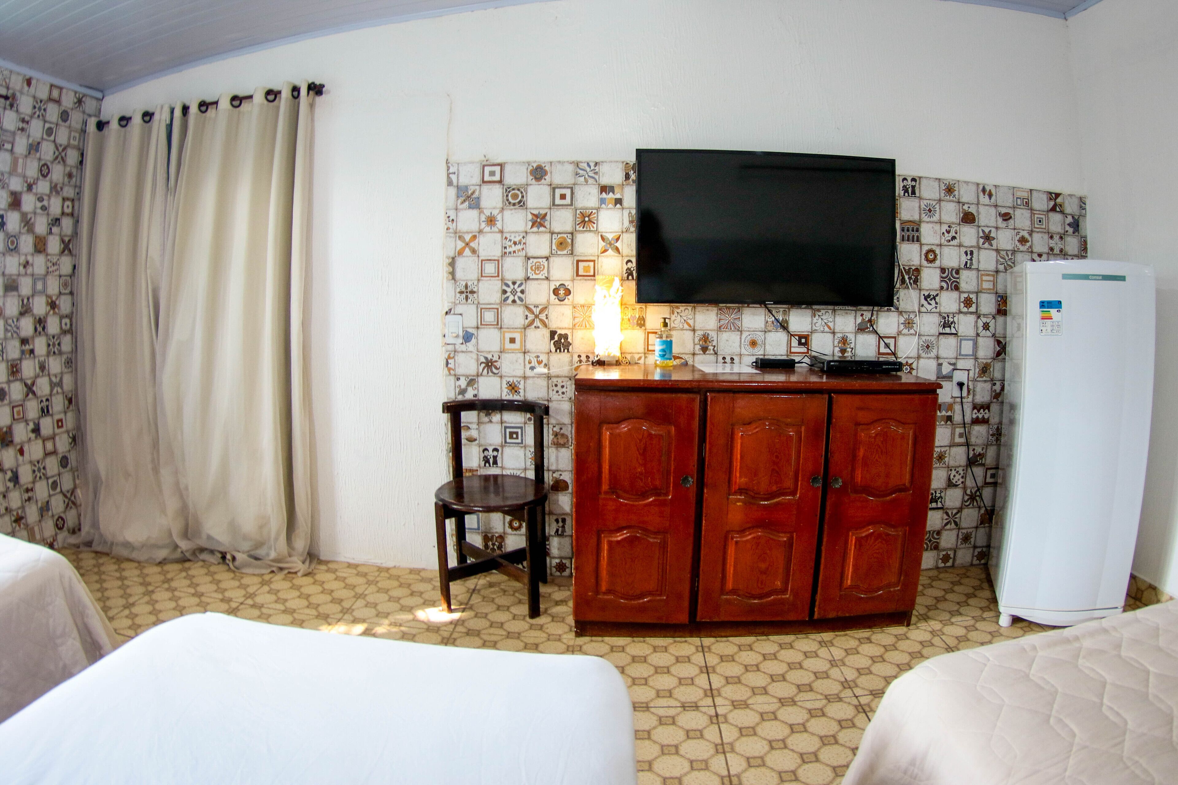 Quarto de hotel com duas camas, televisão, armário, cadeira e frigorífico.