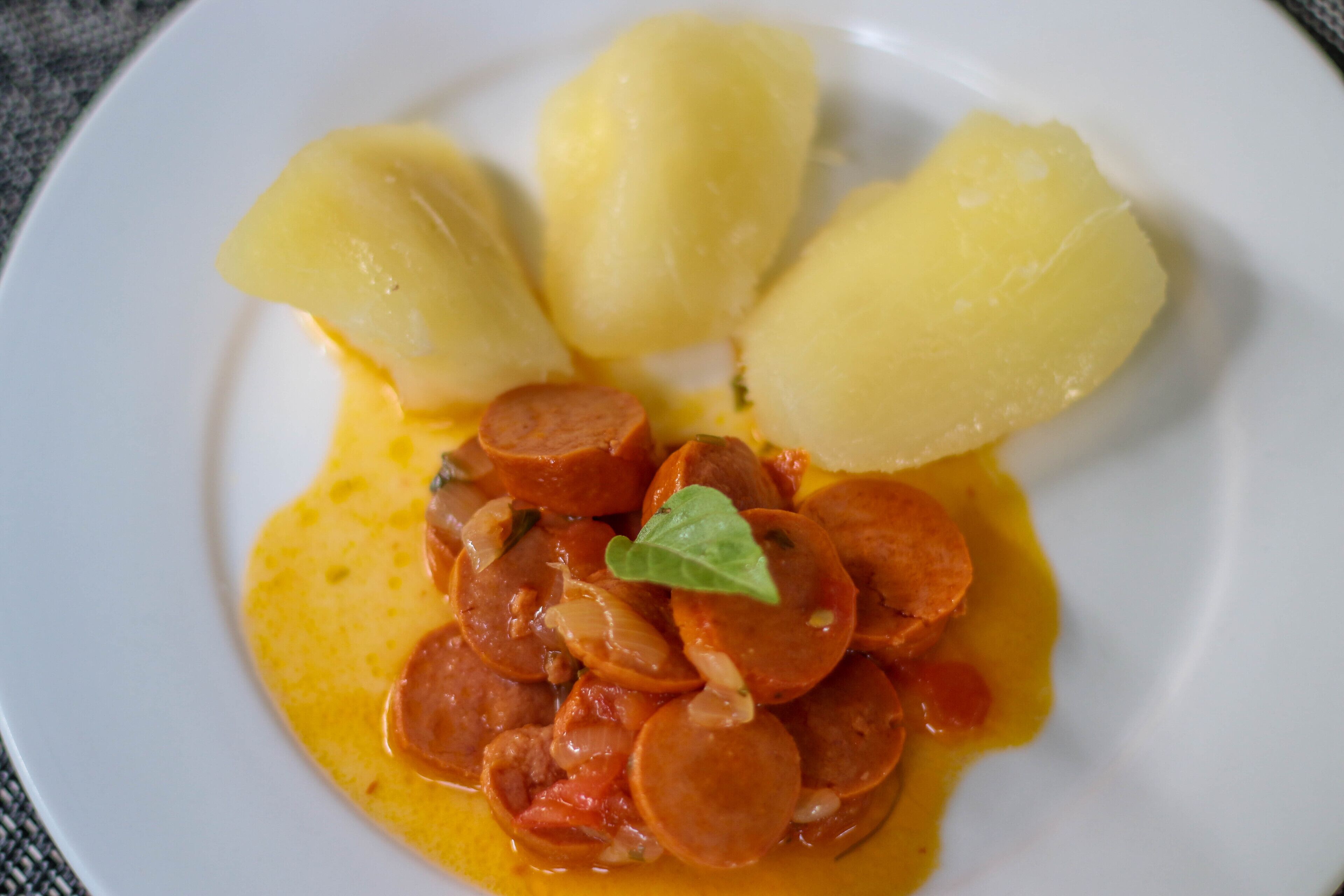 A plate with sliced sausage and boiled potatoes.