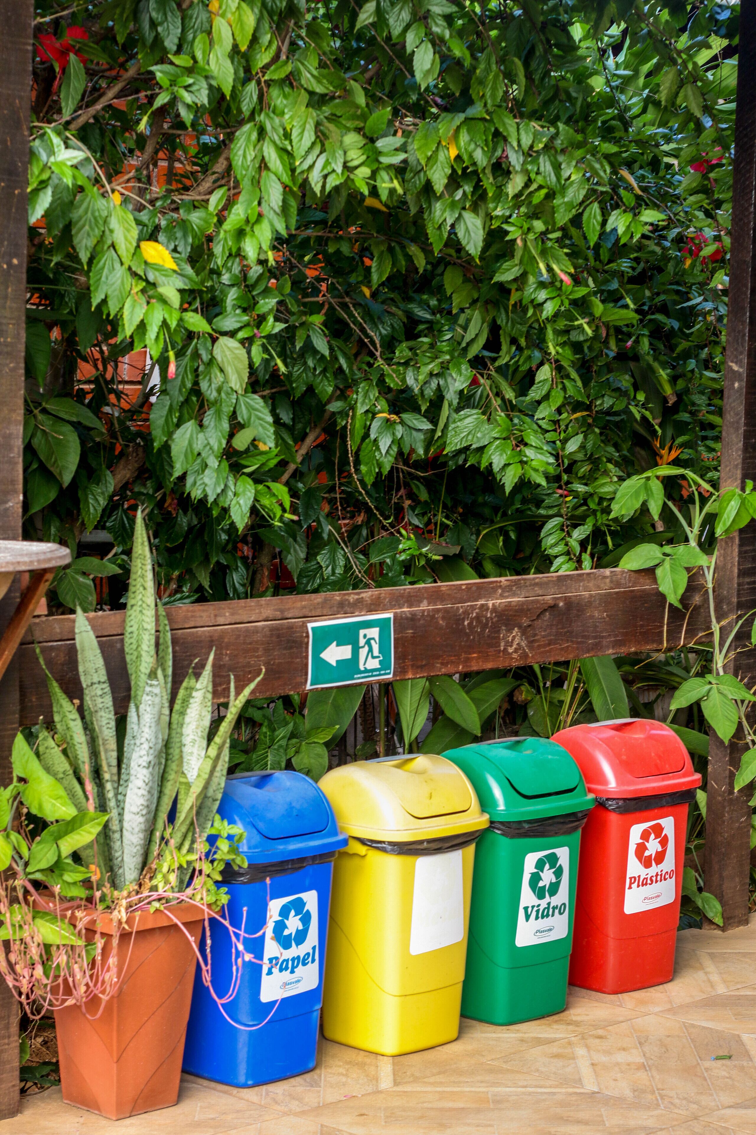 A row of recycling bins in front of a wooden fence with a green arrow sign.