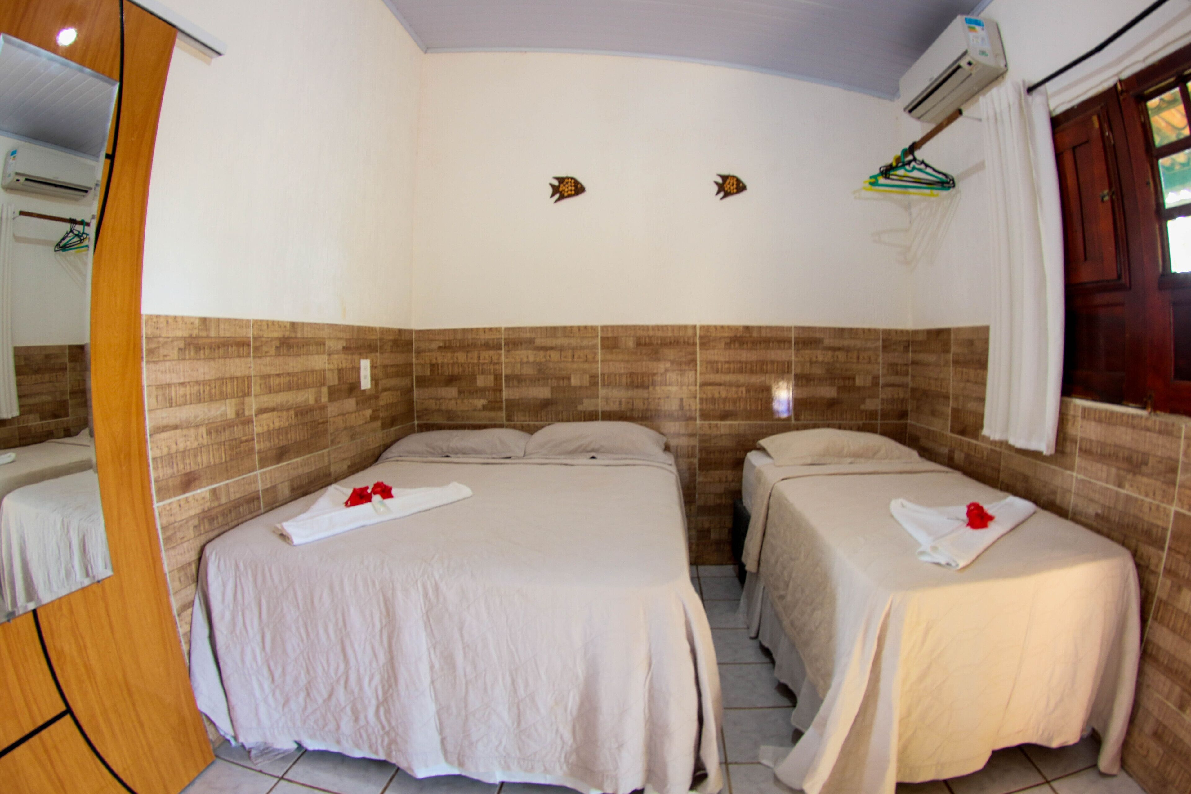 Une chambre d’hôtel avec deux lits, une tête de lit en bois, un climatiseur fixé au mur et une fenêtre avec des rideaux.