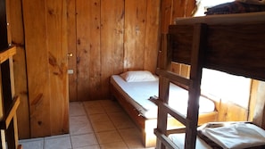 Une chambre dans un chalet en bois, avec un lit simple, une petite table et une fenêtre.