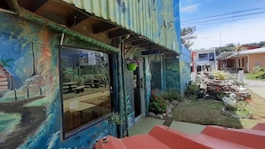 A building with a colorful mural, a visible window, and a small garden area with plants and rocks. - Hostel La Suerte (Monteverde)