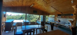 Un intérieur en bois comprenant un coin repas, une cuisine et de grandes fenêtres donnant sur une zone boisée.