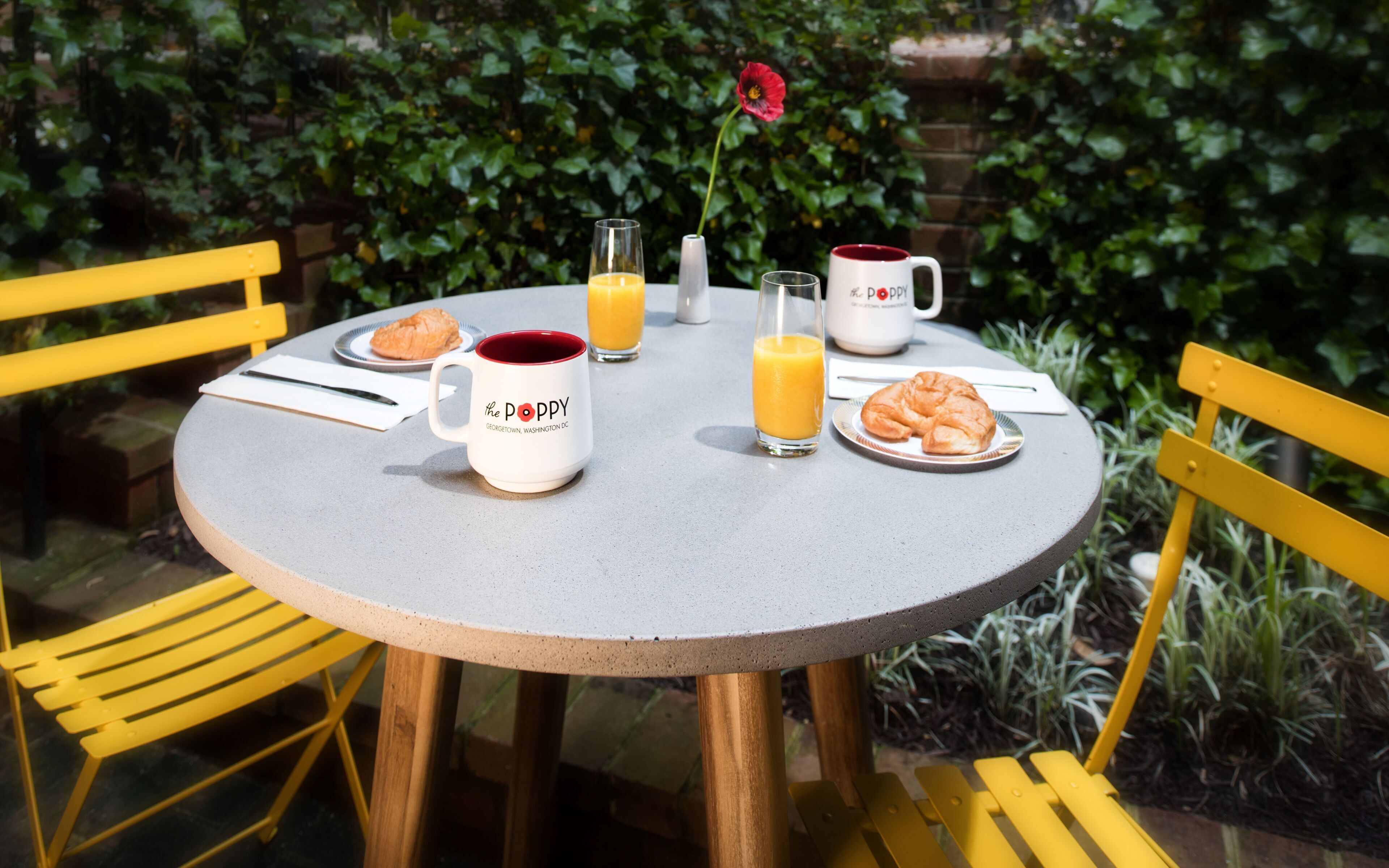 Une table ronde avec une tasse blanche, un verre de jus d’orange, un verre de lait, un croissant et une assiette de croissants.