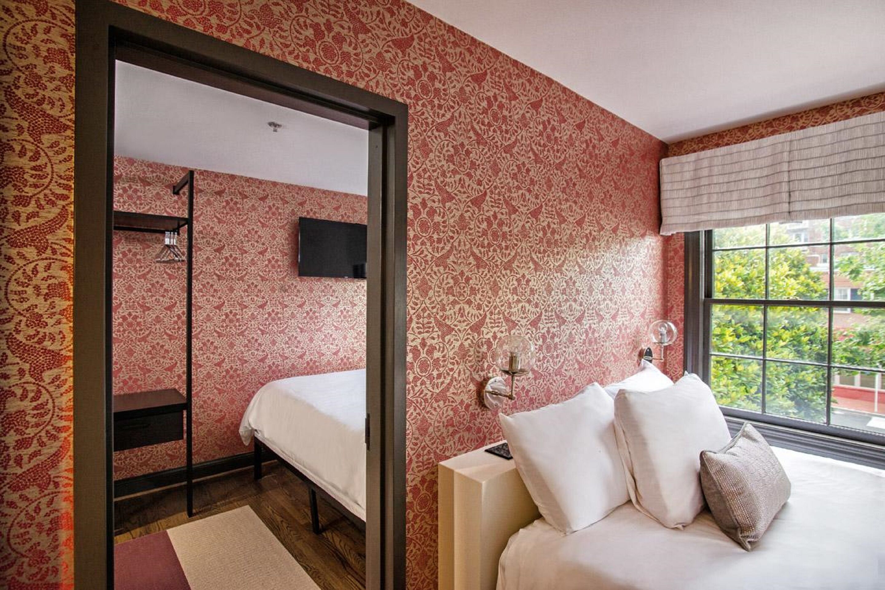 A bedroom with a bed, a nightstand, a TV, and a window with a view.