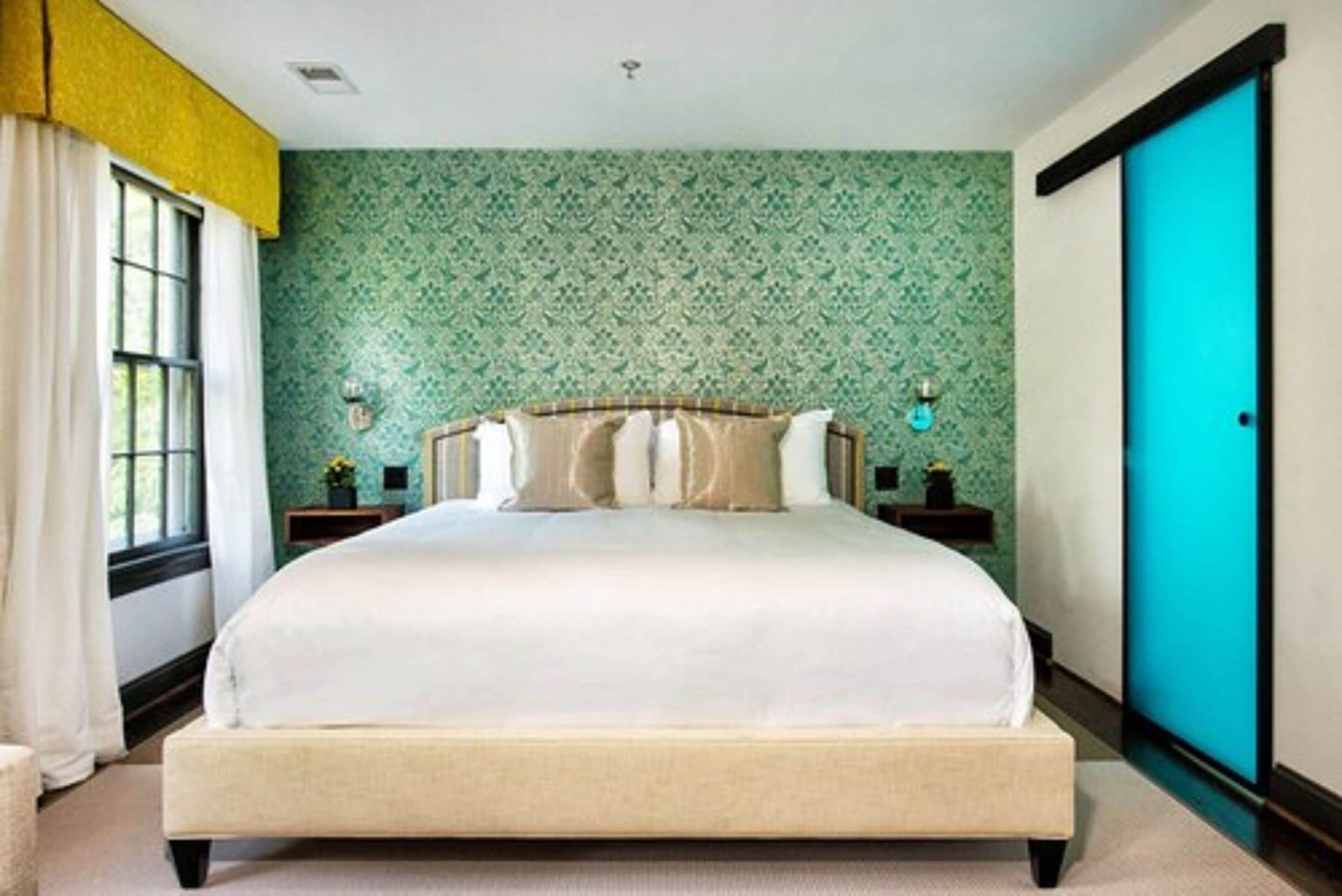 A neatly arranged bedroom with a large bed, a window with curtains, and a green patterned wall.