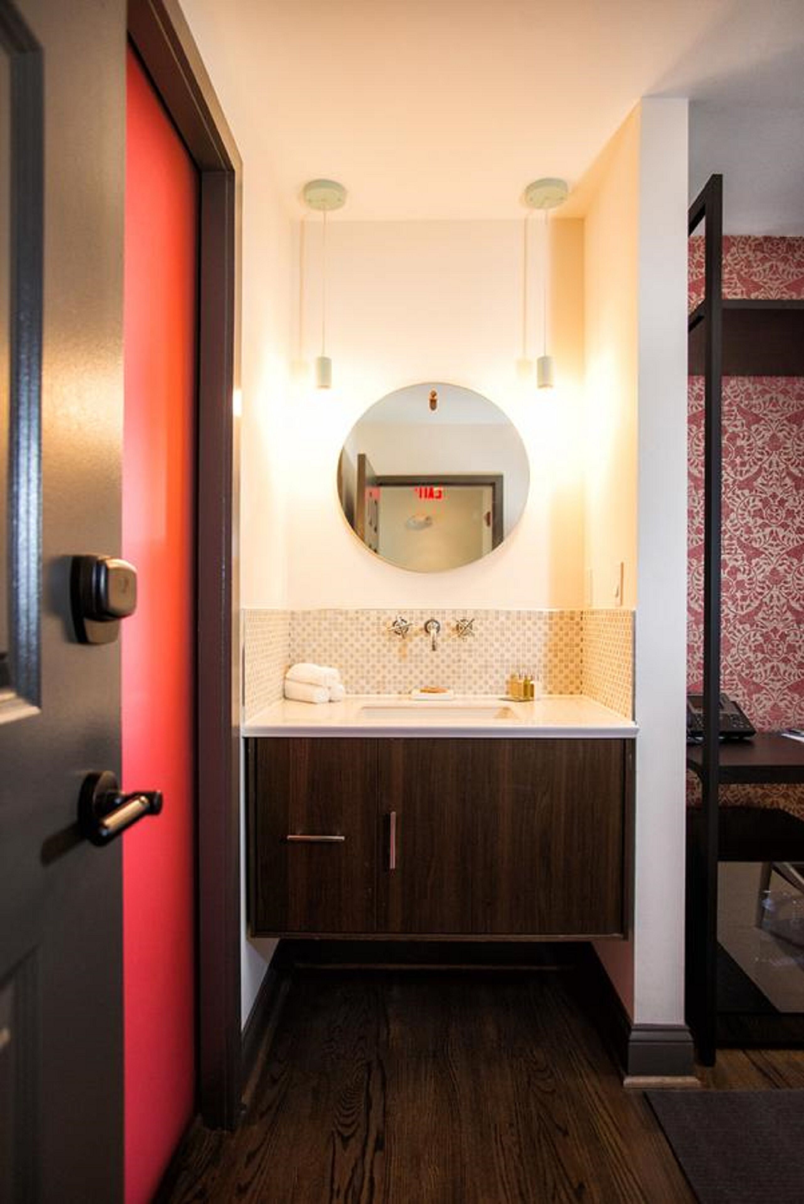 Een badkamer met een ronde spiegel, twee hanglampen, een witte wasbak en een handdoek.