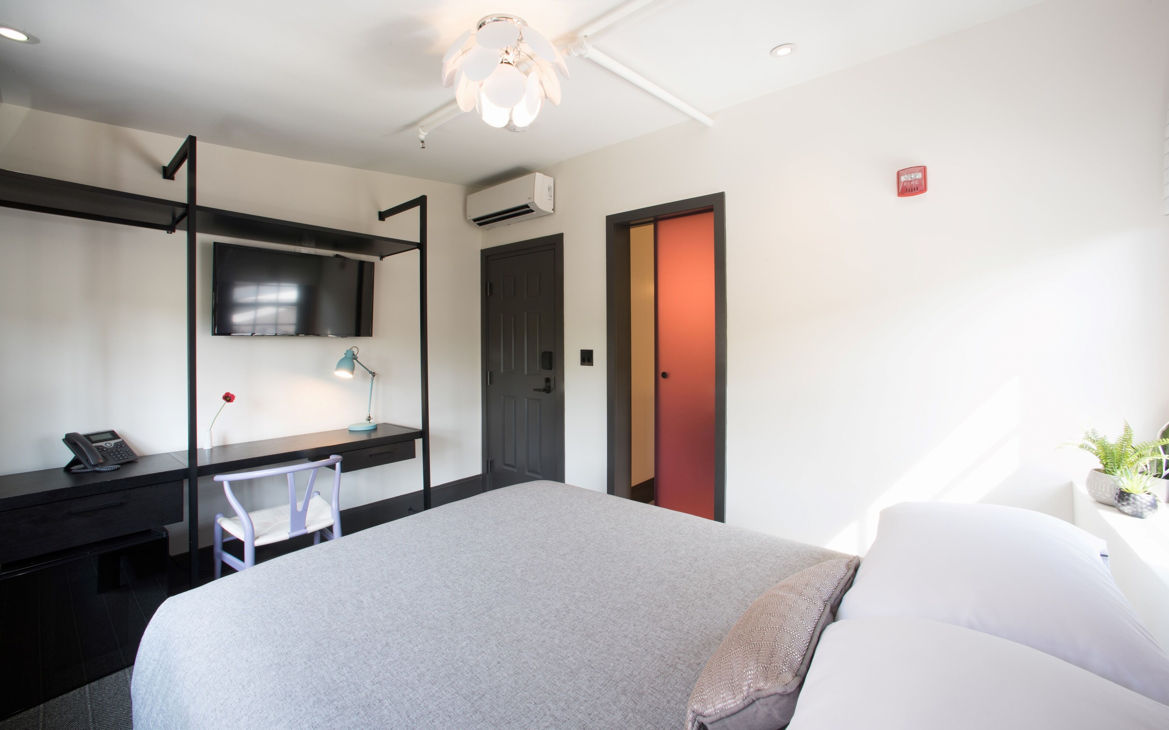 A hotel room with a bed, desk, chair, and a TV on the wall.
