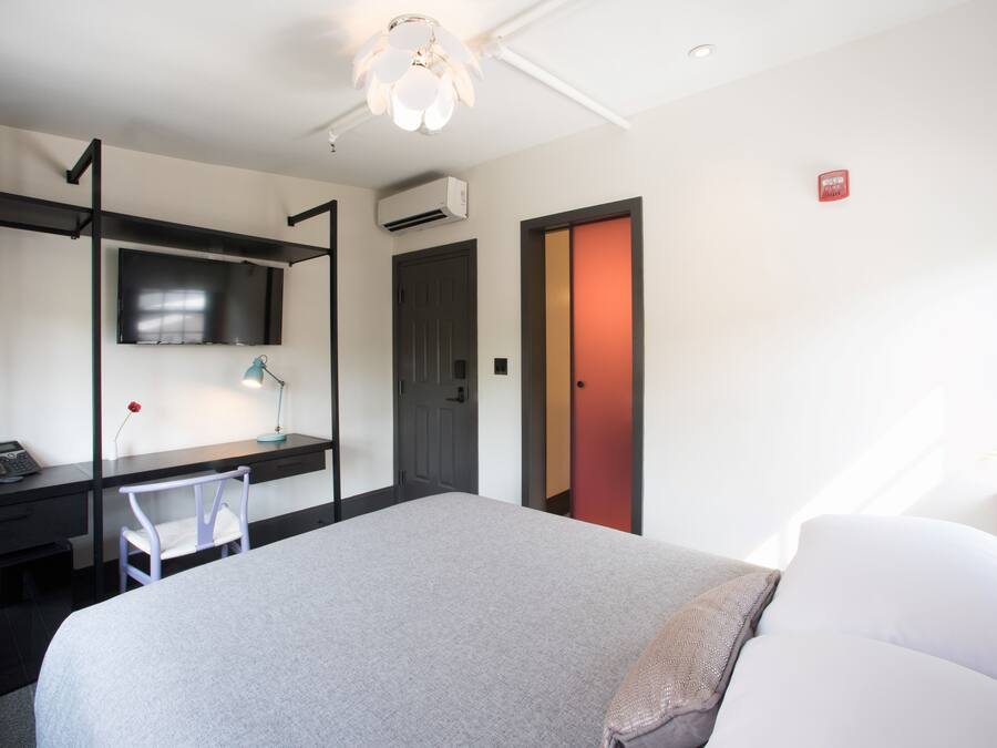 A hotel room with a bed, desk, chair, and a TV on the wall.