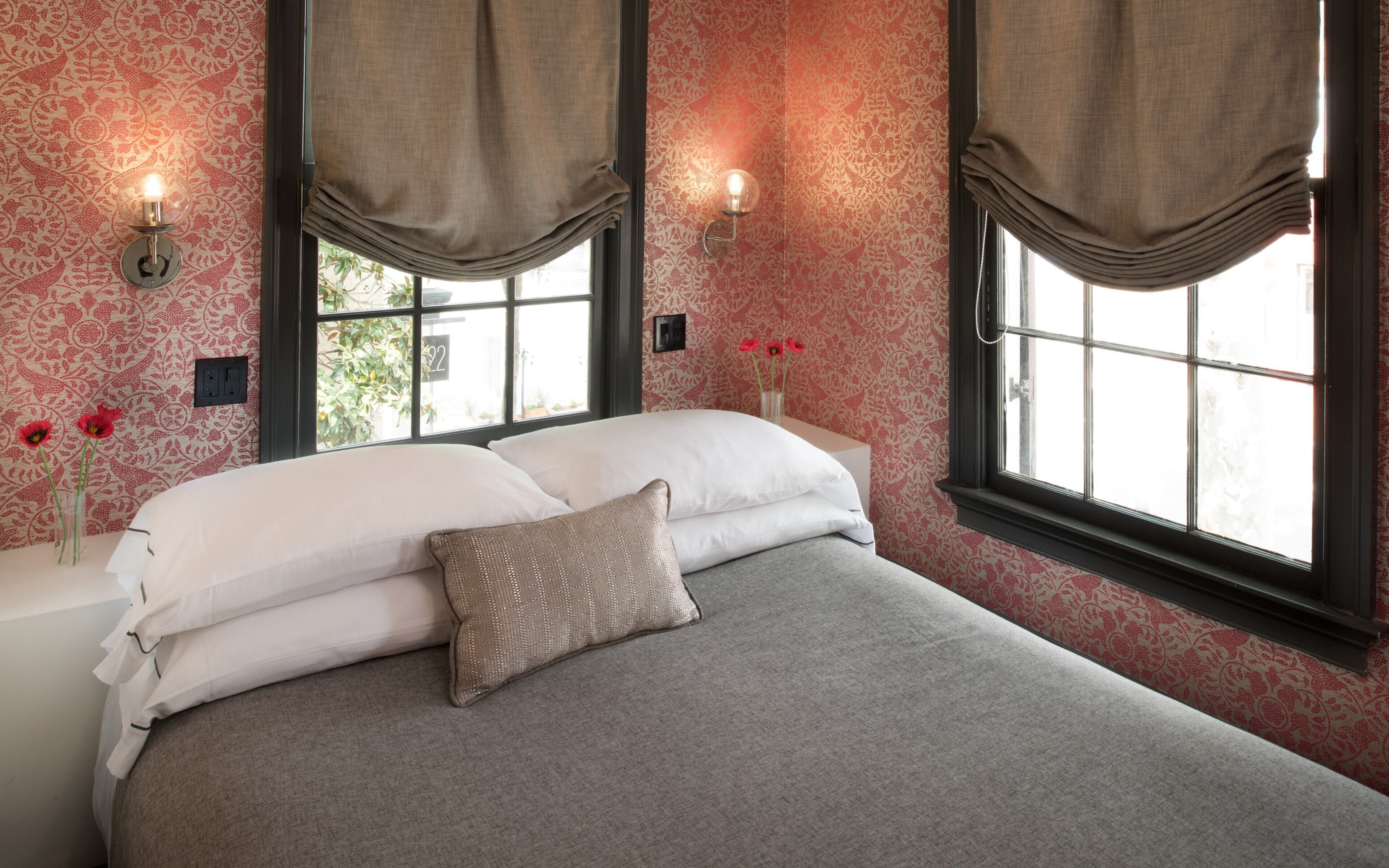 A neatly made bed with white linens and a single decorative pillow, positioned in front of a window with a view of greenery outside.