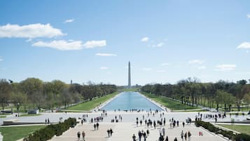 A wide plaza with a central monument, surrounded by trees and a large body of water.