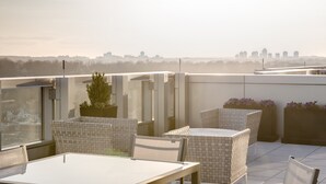 Eine Dachterrasse mit Fliesenboden, Korbmöbeln und Topfpflanzen.