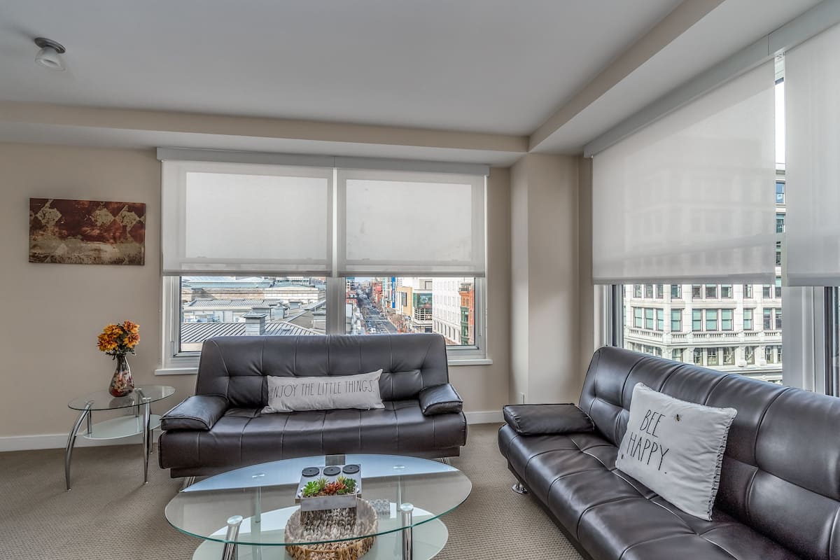 Una sala de estar moderna con dos sofás de cuero, una mesa de centro de vidrio y vistas a la ciudad a través de amplios ventanales.