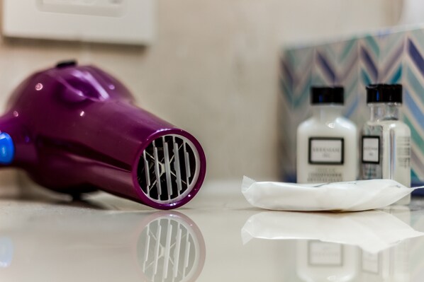 A purple hairdryer, two white bottles, and a white tissue on a reflective surface.