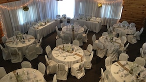 A banquet hall with round tables and white tablecloths, wooden paneling, and string lights. - The Galley Hotel Bar and Grill (Webster)