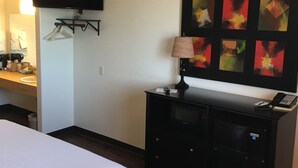A hotel room with a bed, a flat-screen TV mounted on the wall, a dresser with a lamp, and a painting on the wall. - The Galley Hotel Bar and Grill (Webster)