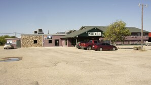 A motel with a stone facade, a green roof, and a parking lot with several cars. - The Galley Hotel Bar and Grill (Webster)