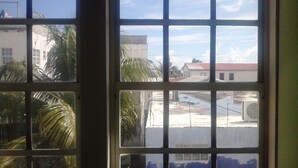 A window with a grid pattern, through which a building with a red roof and palm trees is visible.