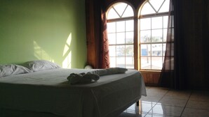 A hotel room with a bed, a window with curtains, and a view of the outside.
