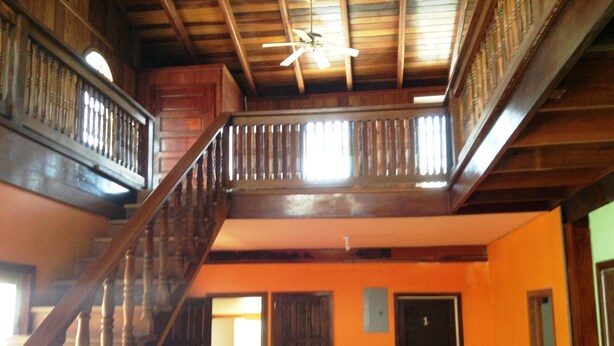 A multi-level wooden staircase with a balcony, connecting different floors of a building with orange walls and wooden ceilings.