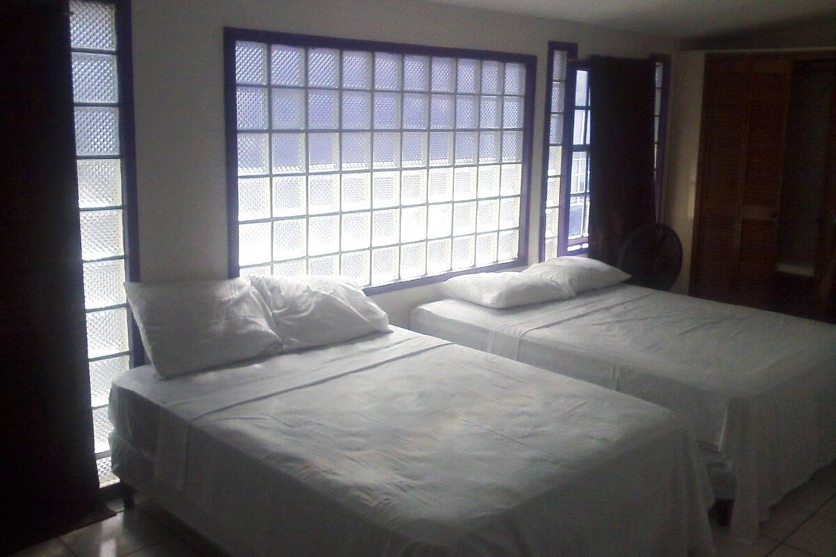 A room with two beds, large windows with blue frames, and a door.