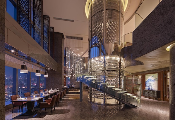 A high-end restaurant with a long dining table, multiple chairs, and a central spiral staircase.