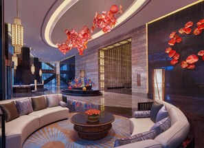 A modern lobby with a curved sofa, a central glass coffee table, and a decorative glass sculpture. - Hilton Haikou (Haikou)