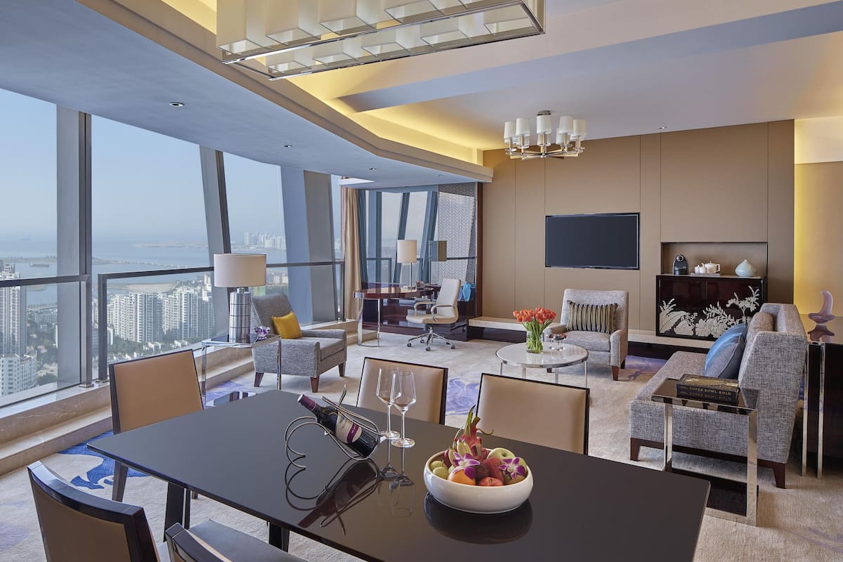 Una habitación de hotel moderna con zona de comedor, asientos, televisor y vista a la ciudad.